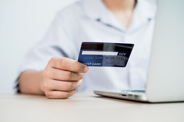 The businesswoman's hand is holding a credit card and using a laptop for online shopping and internet payment in the office