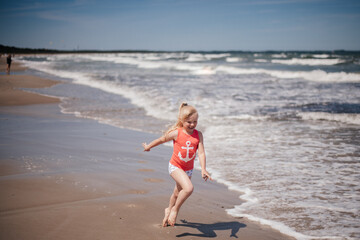 Happy kid girl have fun on sea beach. Funny child run with splashes by water pool along surf edge. Kids activity on summer holiday. Reuniting with nature. Childhood, lifestyle. 