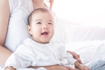 Bright portrait of happy mum holding infant child on hands. Mother hugging her little. happy loving family. mother playing with her baby in the bedroom. Love, trust and tenderness concept.