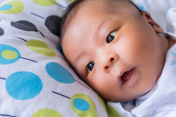 Cute little Asian baby boy lying down on white blanket and looking up camera in the bedroom at home. Breastfeeding or early childhood development concept