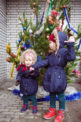 two funny little girls, sisters are standing on the street in winter near the Christmas tree. new year's celebration in the fresh air. tempering and walking.