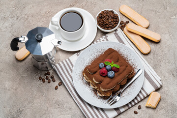 portion of Classic tiramisu dessert with raspberries and blueberries, cup of espresso, coffee maker on grey concrete background