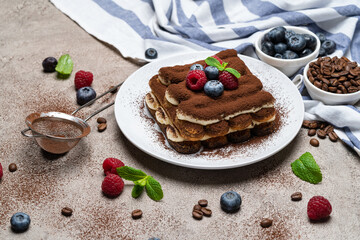 portion of Classic tiramisu dessert with raspberries on grey concrete background