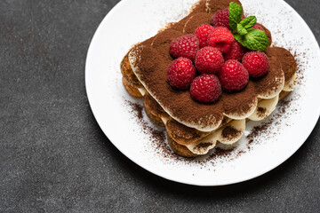 portion of Classic tiramisu dessert with raspberries on dark concrete background
