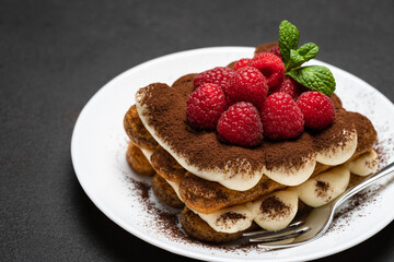 portion of Classic tiramisu dessert with raspberries on dark concrete background