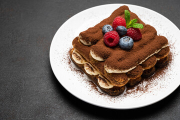 portion of Classic tiramisu dessert with raspberries and blueberries on dark concrete background