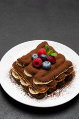 portion of Classic tiramisu dessert with raspberries and blueberries on dark concrete background