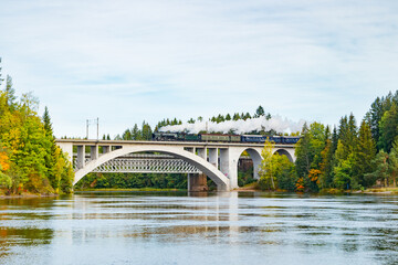 Kouvola, Finland - 18 September 2020: Autumn landscape of bridge with moving old steam passenger train Ukko-Pekka and Kymijoki river waters in Finland, Kouvola, Koria