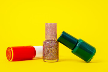 Close up three bottles with nail polishes of different colors, red, golden pink and dark green. Bright yellow background.