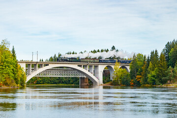 Kouvola, Finland - 18 September 2020: Autumn landscape of bridge with moving old steam passenger train Ukko-Pekka and Kymijoki river waters in Finland, Kouvola, Koria