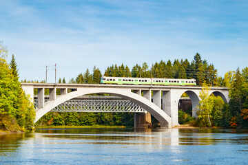 Obraz premium Autumn landscape of bridge with moving passenger train and Kymijoki river waters in Finland, Kouvola, Koria