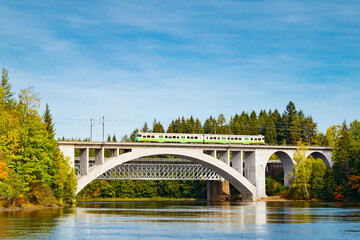 Fototapeta na wymiar Autumn landscape of bridge with moving passenger train and Kymijoki river waters in Finland, Kouvola, Koria