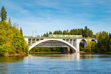 Autumn landscape of bridge with moving passenger train and Kymijoki river waters in Finland, Kouvola, Koria