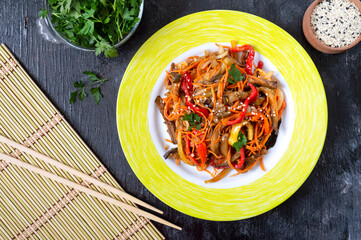 Korean eggplants. Spicy vegetable salad with eggplant, bell peppers, carrots, onions on a plate on a black background.