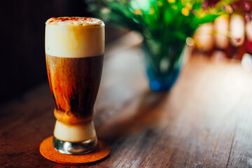 Iced coffee cappuccino   with cream poured over in a tall glass on wooden table