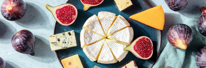 Cheeses panorama, a flat lay with figs, shot from above on a blue background