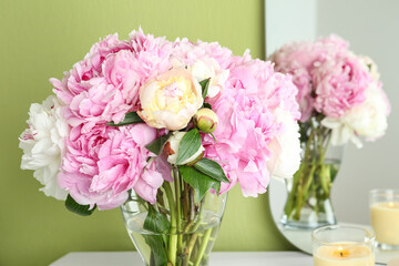 Beautiful peonies and candle on white dressing table near green wall