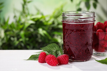 Delicious jam in glass jar and fresh raspberries on white wooden table. Space for text