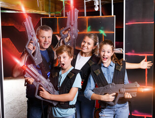 Modern young parents and children with laser pistols posing together at dark laser tag labyrinth