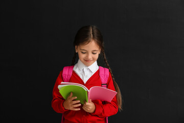 Little schoolgirl with copybook on dark background