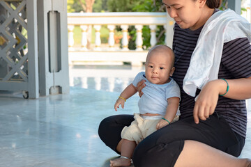 Happy mother and Asian newborn baby boy playing in summer day on the nature. Recreation family concept. Child in beautiful mom embrace cuddling with tenderness. Breastfeeding or development.