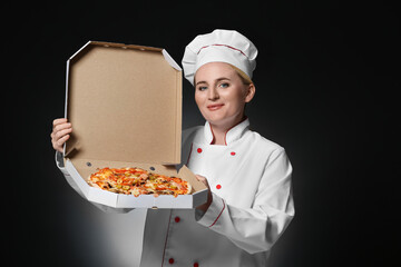 Mature female chef with tasty pizza on dark background