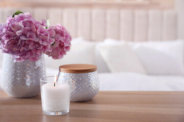 Fototapeta na wymiar Burning candle and beautiful flowers on wooden table indoors. Space for text