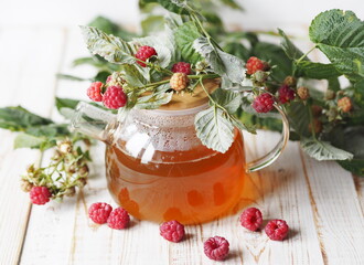 Autumn late raspberries. Useful properties of medicinal tea with raspberries. Branch with raspberries on a glass teapot with tea on a light background.