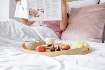 Tray with tasty breakfast on bed of young woman