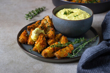 Baked crispy potato wedges with cheese sauce and thyme on black ceramic plate. Homemade snack food.