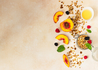Homemade crunchy granola in glass jar, peaches, berries, honey and mint, light concrete background....