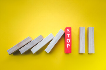 Wooden Blocks With Stop Text Stopping Falling Dominos On yellow. Concept of creative, logical...