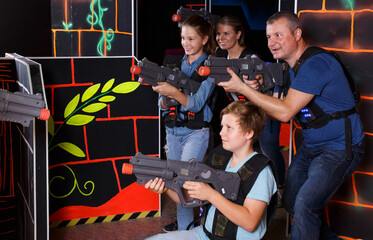 Smiling kids and parents aiming laser guns and playing together laser tag game indoors..