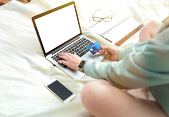 Girl is sitting on a white bed in a room with a credit card and laptop