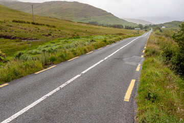Small narrow road without hard shoulder in Connemara, Ireland, Mountains covered with low cloudy sky. Nobody.