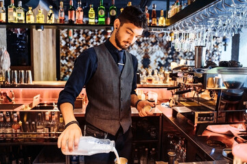 A young Caucasian barista pours milk into coffee espresso, making cappuccino or latte. A professional barista preparing coffee with inspiration on the bar counter