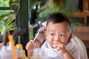 Happy little Asian boy tucking into his lunch and learning to feed himself with family at the...