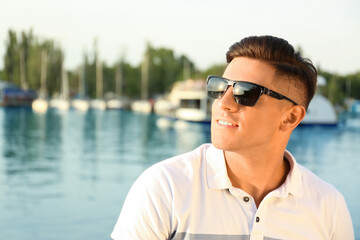 Handsome man wearing stylish sunglasses near river. Space for text