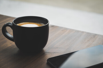 Cup of coffee with cellphone on the table in the cafe. Hot latte with mobile telephone in the office. Natural black mug the best start to any morning about business contacts in the restaurant.