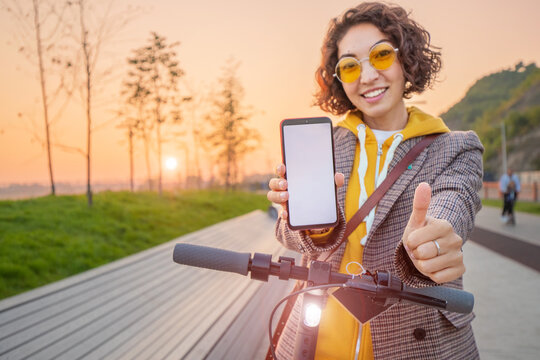woman uses an app on her smartphone to unlock a shared electric scooter on a city street. New eco-friendly transport