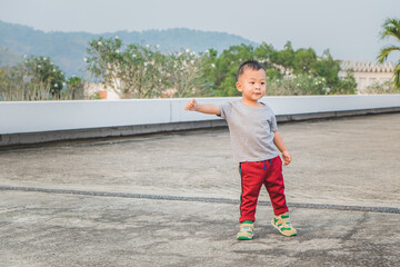 Cute little Asian baby boy standing and raise arm in the public park running for exercise. Living healthy lifestyle.