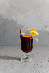 Mulled wine with cinnamon, anise, cloves and orange in glass on a gray background.