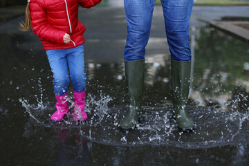 Father and daughter in rubber boots outdoors after rain, closeup