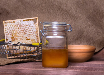 a jar of honey combs in an iron basket and a clay plate on a wooden table against a background of burlap