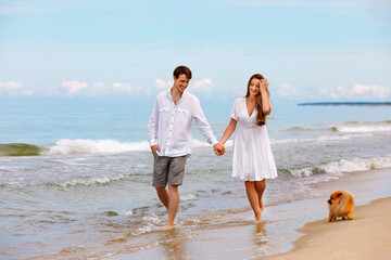 Cute couple of young lovers with a Pomeranian dog walk along the beach