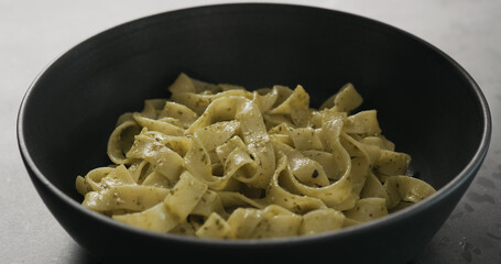 pesto fettuccine in black bowl on concrete countertop