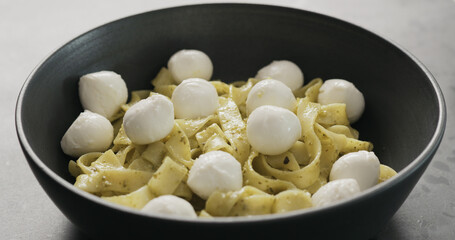 mozzarella with pesto fettuccine in black bowl on concrete countertop