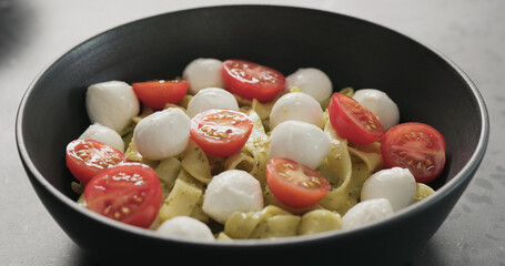 pesto fettuccine with mozzarella and tomatoes from black bowl on concrete countertop