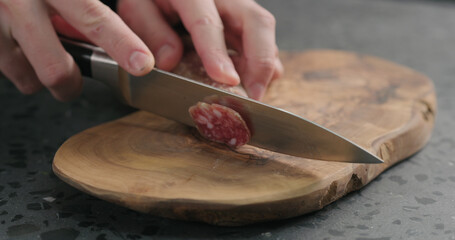 man slicing fuet sausage on olive wood board