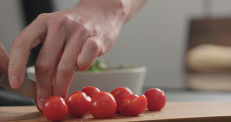 closeup man cutting cherry tomatoes on olive board